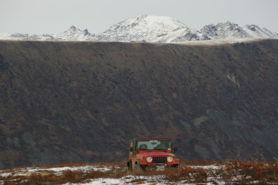 Red 2003 Jeep TJ parked in a field with snow and brown brush, mountains in background
