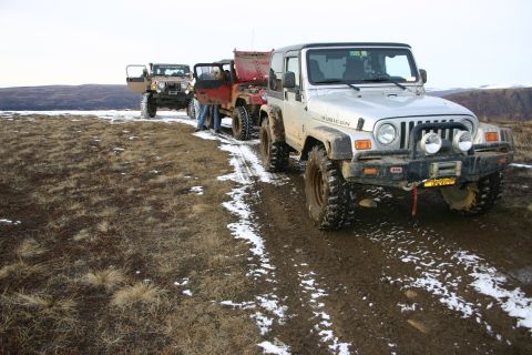 2003 Jeep TJ - Three Jeep Wranglers drive in a line on a muddy and snowy trail with hills in the background.
