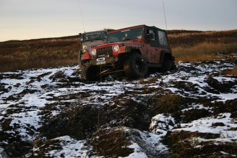 2003 Jeep TJ - Two Jeep Wranglers navigate a challenging muddy and snowy landscape, with one vehicle deeply mired.