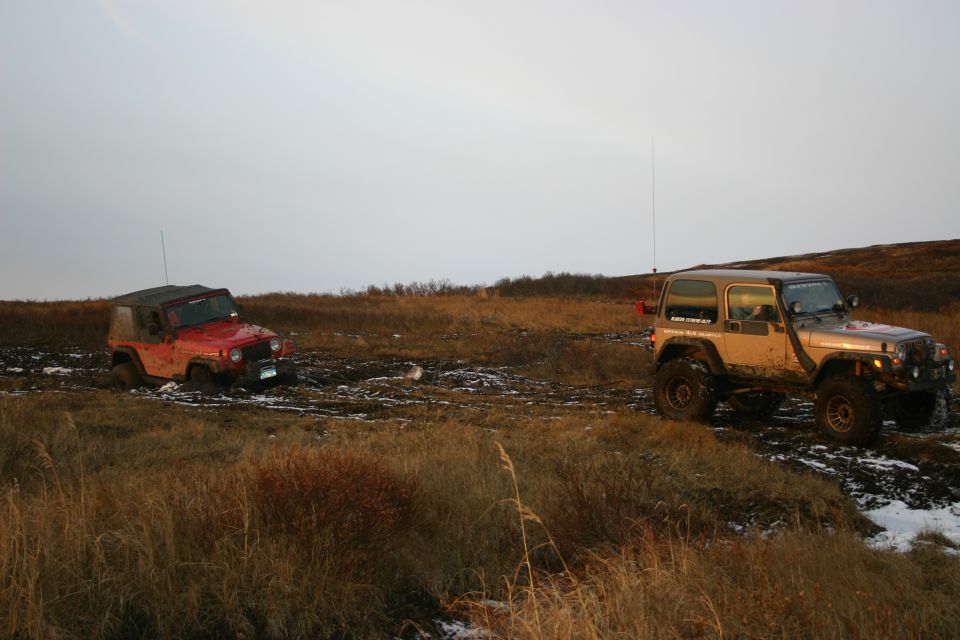 Two Jeeps, one stuck in mud, the other pulling it out on a dirt trail