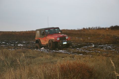 2003 Jeep TJ - A red 2003 Jeep TJ is stuck in a muddy field under an overcast sky.