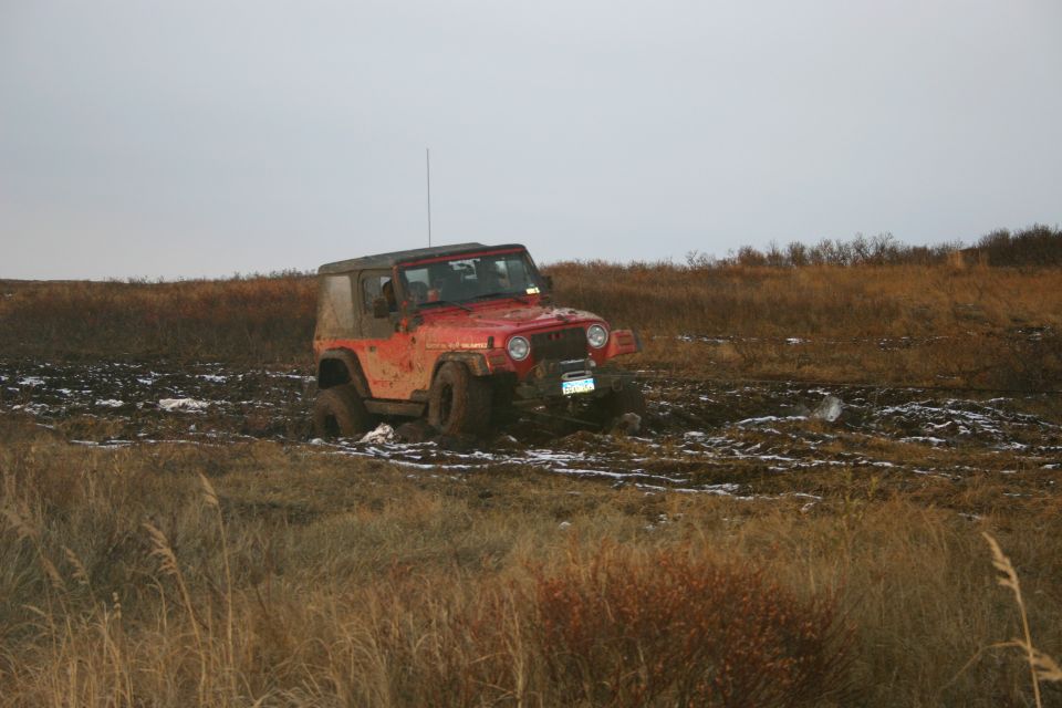 Red 2003 Jeep TJ stuck in muddy terrain with dry grass and overcast sky