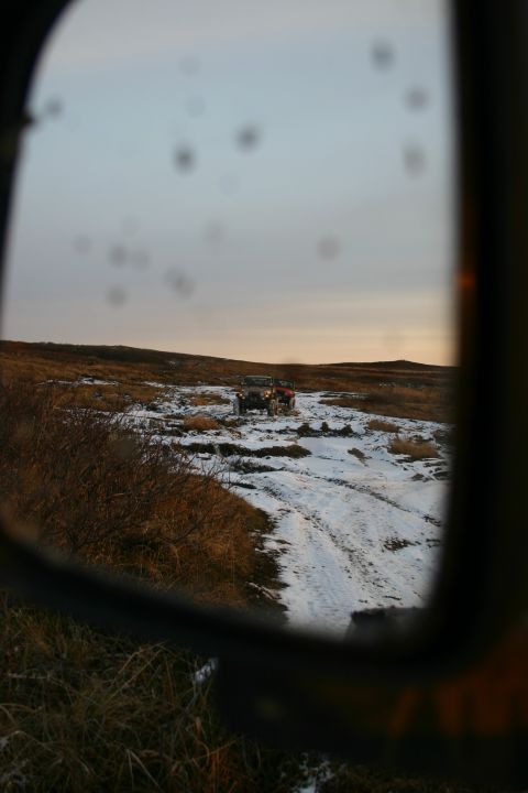 2003 Jeep TJ - Two off-road vehicles navigate a snowy, rutted path through a barren landscape, as seen reflected in a side mirror.