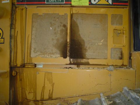 1966 International School Bus - Close-up of a yellow heavy equipment's engine compartment, showing mesh screens and signs of oil leakage.