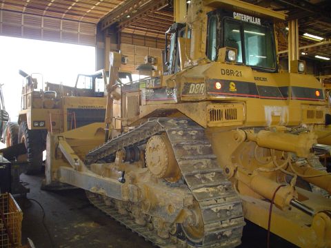 1966 International School Bus - A yellow Caterpillar D8R bulldozer, identified as D8R-21, is parked indoors next to a Caterpillar dump truck.
