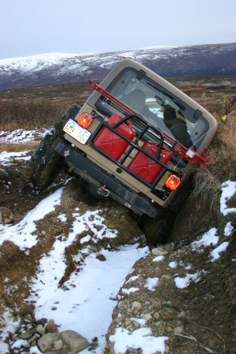 2003 Jeep TJ - A Jeep TJ is stuck in a ditch during an off-road excursion with snow on the ground and mountains in the background.