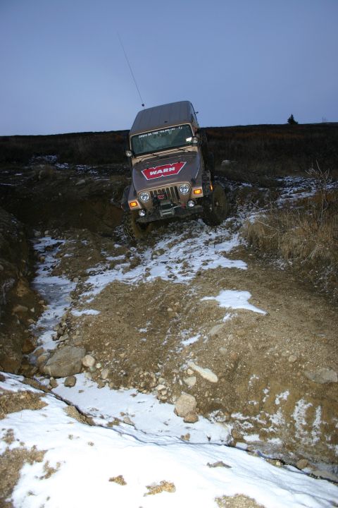 2003 Jeep TJ - A Jeep TJ navigates a challenging off-road trail with patches of snow and mud.