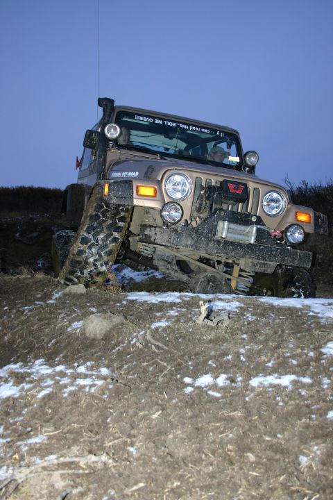 2003 Jeep TJ - A tan 2003 Jeep TJ navigates a challenging muddy and snowy incline during daylight.