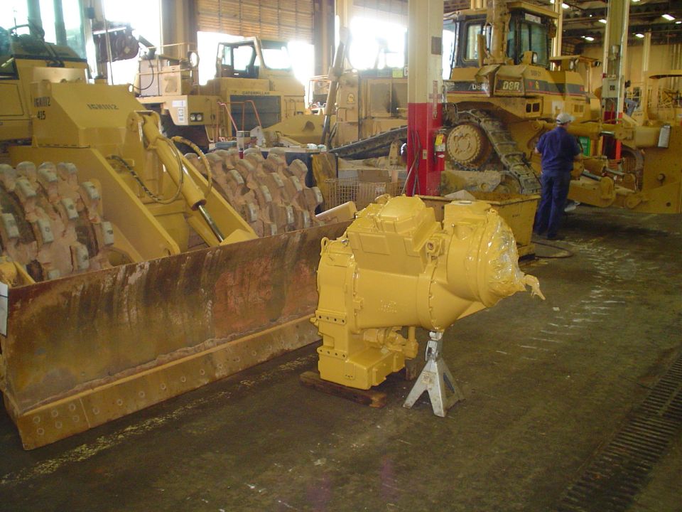 Yellow transmission on jack stands, heavy equipment in shop