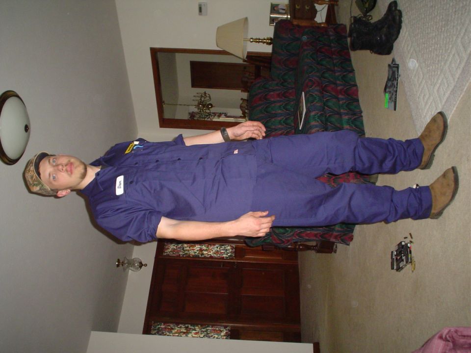 Person in blue overalls and camouflage hat standing indoors