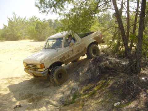 1989 Ford Bronco - A tan Ford Bronco navigates a sandy and muddy incline during an off-road excursion.