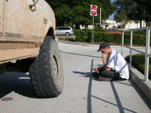 1989 Ford Bronco - A mud-covered 1989 Ford Bronco is shown from the side, with a person sitting on the curb nearby.