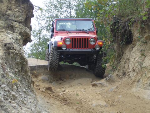 1990 Ford Bronco - A red Jeep Wrangler tackles a challenging off-road path with steep, eroded sides.