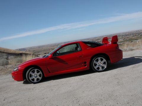 1999 Mitsubishi 3000GT - Side view of a red 1999 Mitsubishi 3000GT sports car on a dirt road.