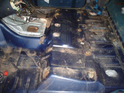 1984 Ford Bronco - The interior floor of a vehicle shows signs of rust and exposed wiring, indicating a need for repair.