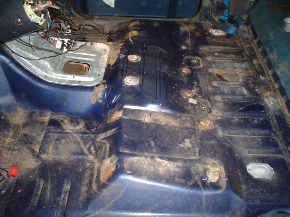 Blue vehicle interior floor with rust and exposed wiring