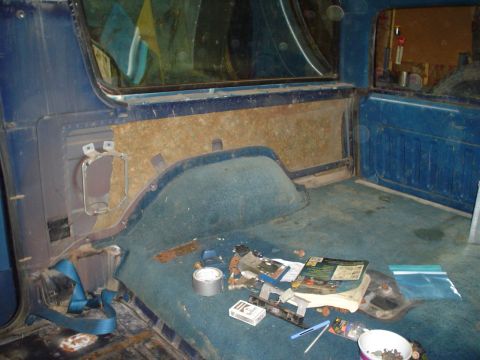 1984 Ford Bronco - The interior of a blue SUV shows blue carpet and door panels, with some debris on the floor.