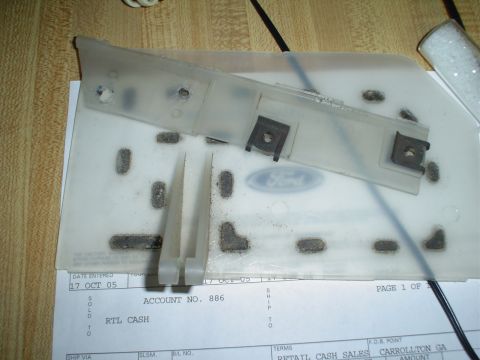 1984 Ford Bronco - A clear plastic part with a Ford emblem and metal clips sits on top of a document.