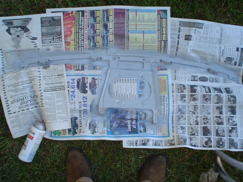Spray can next to a gray painted car part laid out on newspapers