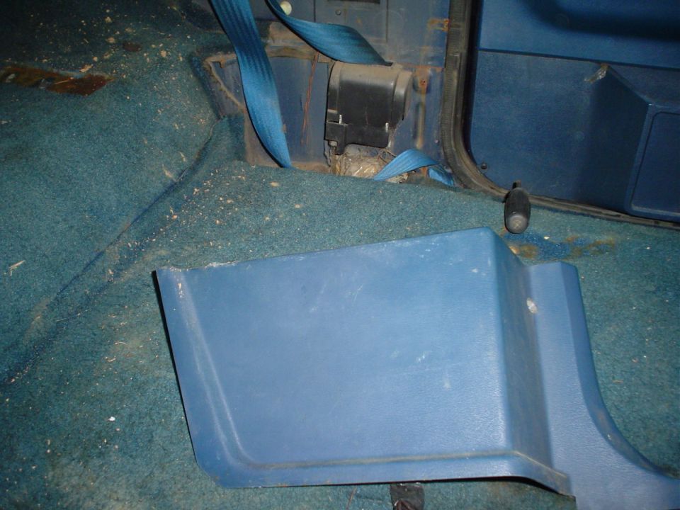 Blue carpet and plastic trim inside a vehicle, with a blue seatbelt mechanism visible