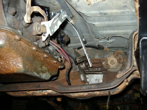 1985 Ford Bronco - Underbody view of a vehicle's transmission shifter linkage mechanism, showing rusty parts.