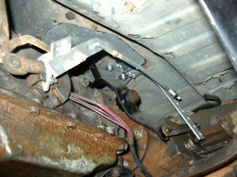 1985 Ford Bronco - Close-up of the shifter linkage mechanism and associated wiring underneath a vehicle.