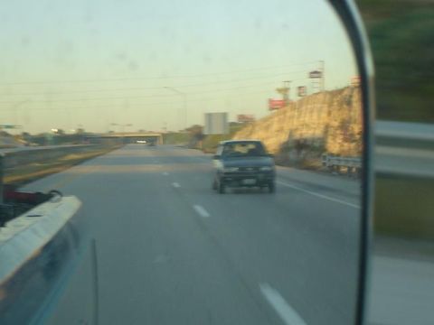 1979 Ford Bronco - A dark sedan travels down the highway, reflected in a side mirror. The Supermotors.net logo is visible in the corner.