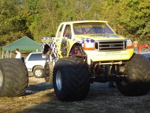 1979 Ford Bronco - A yellow monster truck with custom graphics sits on a grassy area next to a white SUV.