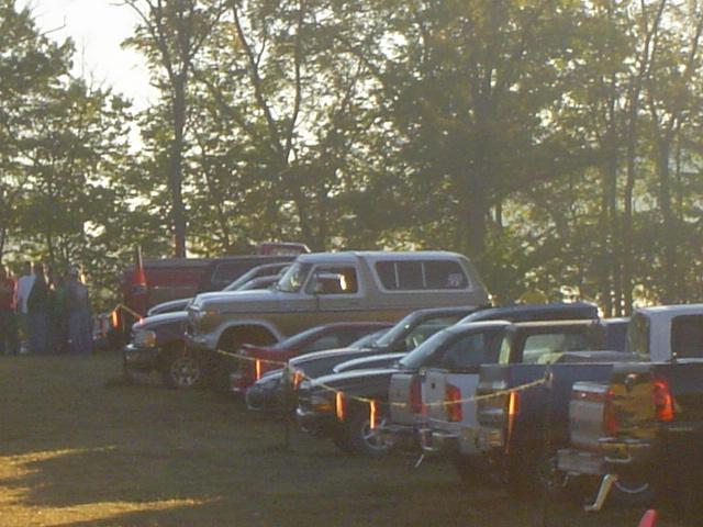Gray 1978 Ford Bronco with gold trim parked in a grassy field with trees and other vehicles