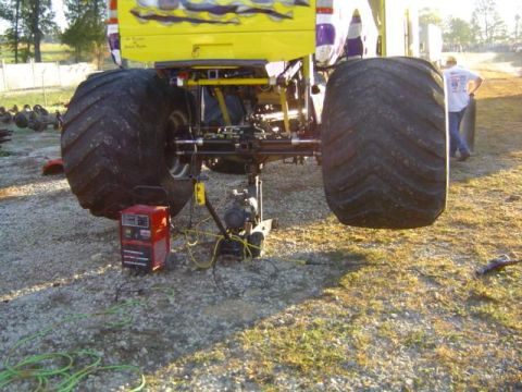 1979 Ford Bronco - A monster truck's massive rear tires and suspension are visible, with a welding machine connected nearby.