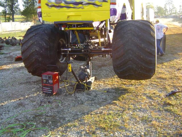Monster truck rear axle with large tires and a red welding machine