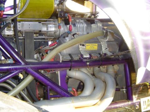 1979 Ford Bronco - This custom engine features a prominent supercharger and a complex exhaust system, with a yellow sticker from "Malain's Automotive" visible.