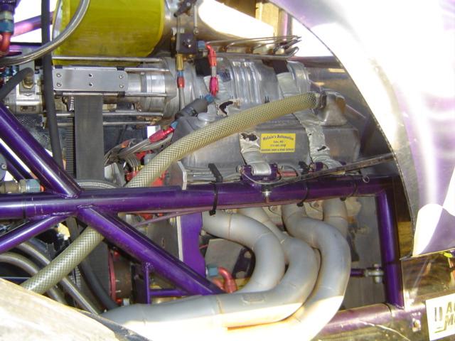 Close-up of a supercharged engine with purple roll cage and custom exhaust pipes