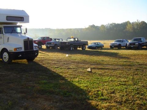 1979 Ford Bronco - A collection of vehicles are parked in a field at sunrise, with trees in the background.