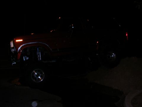 1984 Ford Bronco - A red SUV with a lifted suspension is seen at night, with its front turn signal illuminated.