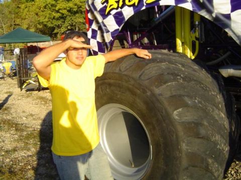 1979 Ford Bronco - A person stands next to a giant monster truck tire, shielding their eyes from the sun.