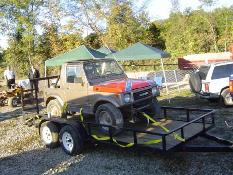 1979 Ford Bronco - A Suzuki Samurai is loaded onto a trailer, with a white SUV parked nearby under tents.