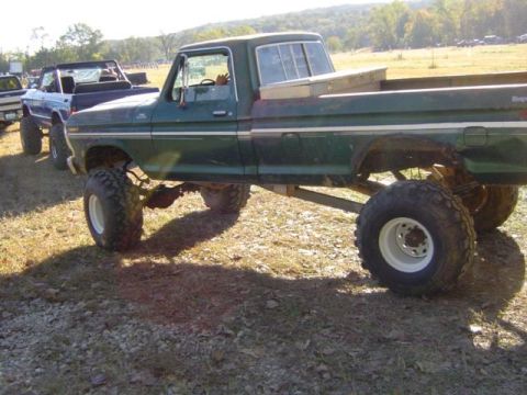 1979 Ford Bronco - A lifted green pickup truck is parked in a field alongside other vehicles.