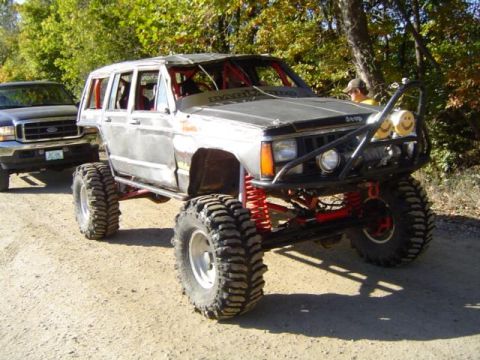 1979 Ford Bronco - A heavily modified Jeep Cherokee sits off-road, with a Ford truck visible behind it.