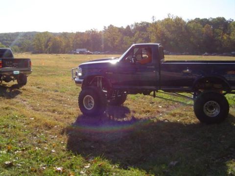 1979 Ford Bronco - A heavily modified pickup truck sits in a grassy field, with another truck visible in the distance.