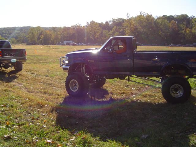 Lifted dark blue pickup truck side view, another truck in background