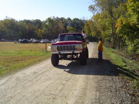 1979 Ford Bronco - A lifted red 1979 Ford Bronco parked on a dirt road during an outdoor event.