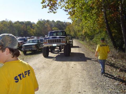 1979 Ford Bronco - A lifted pickup truck is parked on a dirt road, with other vehicles and staff members visible.