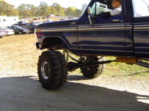 1979 Ford Bronco - A lifted 1979 Ford Bronco pickup truck with oversized tires is parked outdoors with other vehicles in the background.