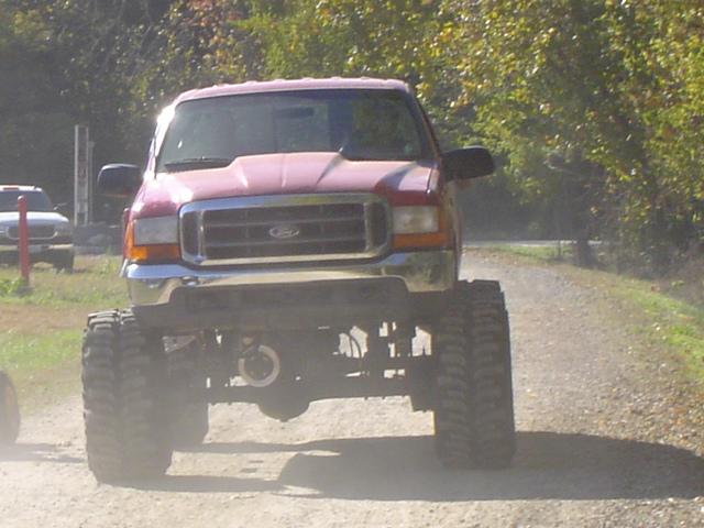 Red Ford truck with huge tires driving on a dirt road