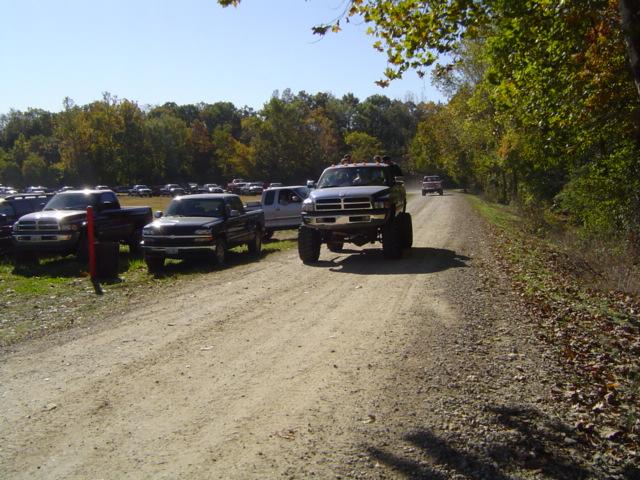 Lifted pickup truck driving on dirt road, other trucks parked nearby