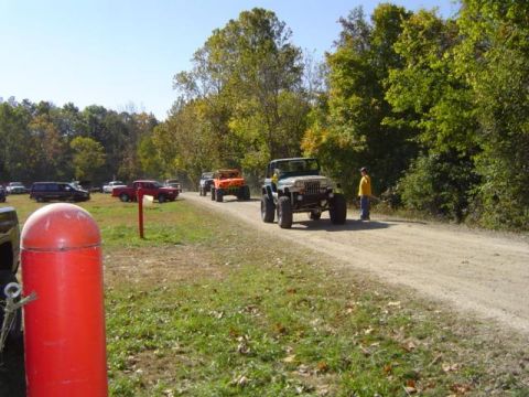 1979 Ford Bronco - Several off-road vehicles are gathered on a dirt road surrounded by trees, with a green Jeep Wrangler prominently featured.