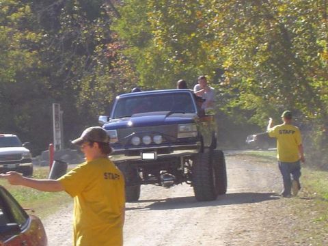 1979 Ford Bronco - A lifted blue truck is the main focus, with staff members directing traffic at an outdoor event.