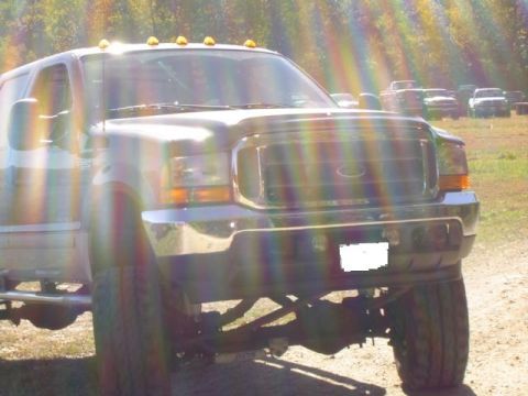 1979 Ford Bronco - Front view of a lifted Ford truck with a chrome grille. Several other vehicles are visible in the background.