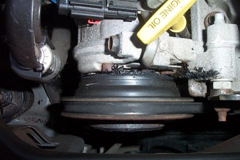 1999 Chrysler 300M - The engine's pulley system shows significant wear and damage, with a broken belt and debris accumulation.
